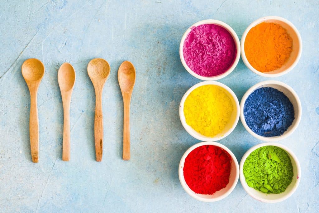 "Colorful arrangement of wooden spoons and bowls of powdered pigments for Holi festival celebration."